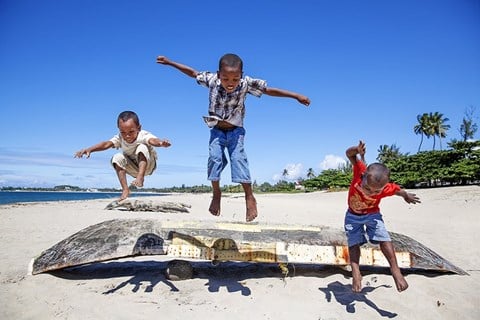 tři chlapci přeskakující loďku na mořském pobřeží
